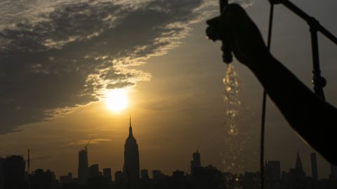 The sun rises over New York City and the Empire State Building while a man sprays water at Pier A.