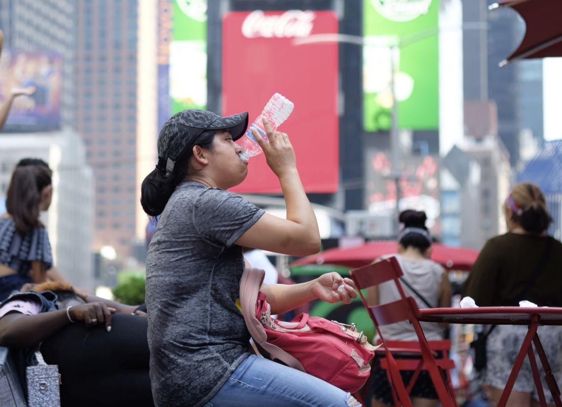 A woman drinks water in Times Square as temperatures reach the mid-to-upper 90s.