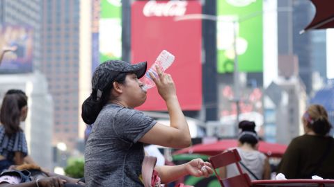 A woman drinks water in Times Square as temperatures reach the mid-to-upper 90s.