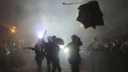 A broken umbrella flies by near riot police, during confrontation with protesters in Hong Kong Sunday, July 21, 2019. Hong Kong police launched tear gas at protesters Sunday after a massive pro-democracy march continued late into the evening. The action was the latest confrontation between police and demonstrators who have taken to the streets to protest an extradition bill and call for electoral reforms in the Chinese territory. (Andy Lo/HK01 via AP)