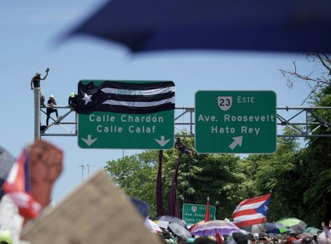 Protesters attach a banner to a highway sign.