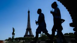 TOPSHOT - A man holding a bottle of water walks by a woman sipping a drink through a straw on a bridge over the Seine river in front of the Eiffel Tower in Paris on July 23, 2019. - Parisians were bracing for potentially the hottest ever temperature in the French capital this week as a new heatwave blasted into northern Europe that could set records in several countries. (Photo by Philippe LOPEZ / AFP)        (Photo credit should read PHILIPPE LOPEZ/AFP/Getty Images)