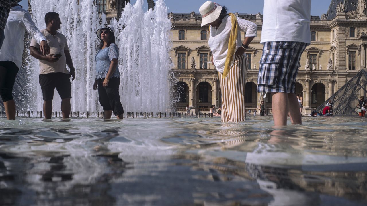 People cool off next to the fountains at the Louvre Museum in Paris.