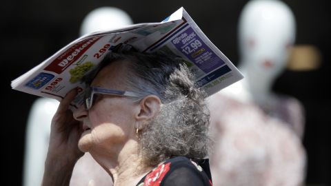An elderly woman shelters from the hot sun with a newspaper, in Milan, Italy.