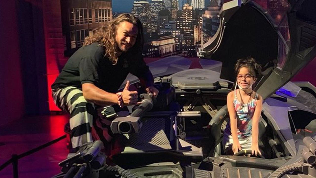 Jason Momoa and a young fan hop into the Batmobile.