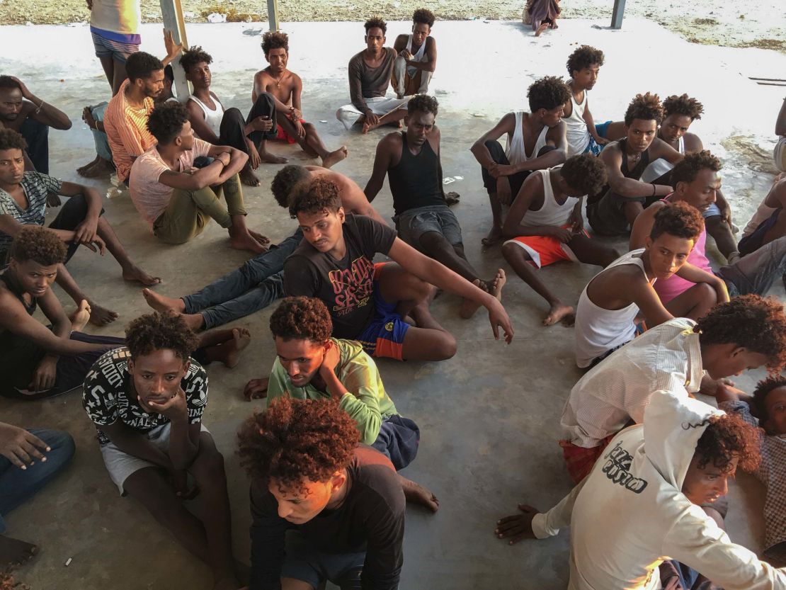 Rescued migrants sit on a coast some 100 kilometers east of Tripoli, Libya, Thursday.