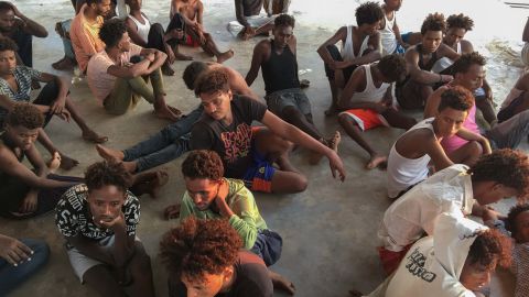 Rescued migrants sit on a coast some 100 kilometers east of Tripoli, Libya, Thursday.
