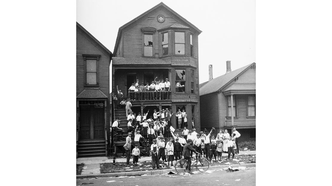 In this 1919 photo provided by the Chicago History Museum, a crowd gathers at a house that has been vandalized and looted during the race riots in Chicago. Some of the crowd is posing inside broken windows, others are standing on the lawn.