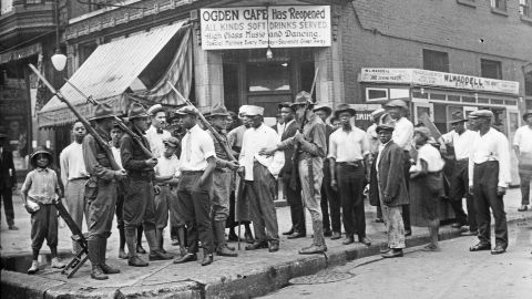 In this 1919 photo provided by Chicago History Museum, a crowd of men and armed National Guard stand in front of the Ogden Cafe during race riots in Chicago.
