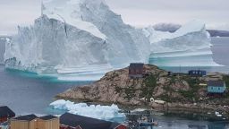 A picture taken on July 13, 2018 shows an iceberg behind houses and buildings after it grounded outside the village of Innarsuit, an island settlement in the Avannaata municipality in northwestern Greenland. (Photo by MAGNUS KRISTENSEN / Ritzau Scanpix / AFP) / Denmark OUT        (Photo credit should read MAGNUS KRISTENSEN/AFP/Getty Images)