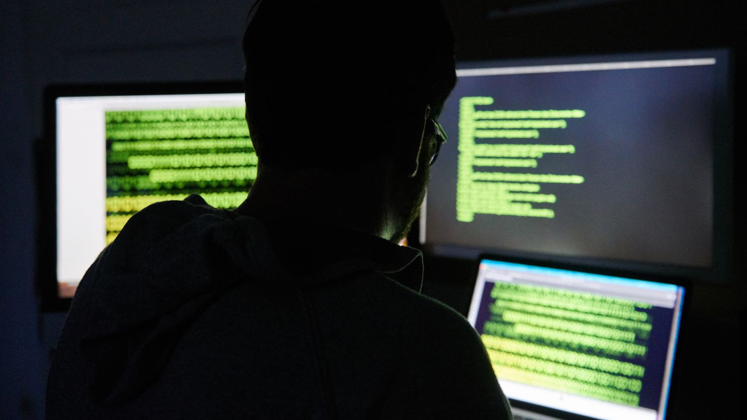  A man sits in front of three screens with text. 