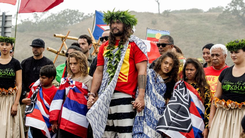 Actor Jason Momoa holds the hands of his children, Nakoa-Wolf Momoa, left, and Lola Momoa, right, as he is welcomed with a hula while visiting elders and Native Hawaiian protesters blocking the construction of a giant telescope on Hawaii's tallest mountain, at Mauna Kea Access Road on Wednesday, July 31, 2019, in Mauna Kea, Hawaii.  (Hollyn Johnson/Hawaii Tribune-Herald via AP)
