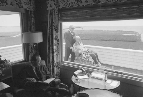 A man in Hyannis Port glances outside a window to see Joseph Sr. being pushed in a wheelchair in 1964. Joseph Sr., a former US ambassador to the United Kingdom, died in 1969.