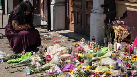 A woman kneels near candles and flowers placed outside Ned Peppers.