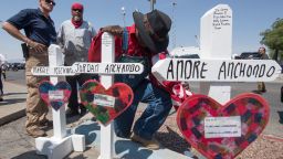 A man prays beside crosses with the names of Jordan and Andre Anchondo, and the other victims of the El Paso massacre.