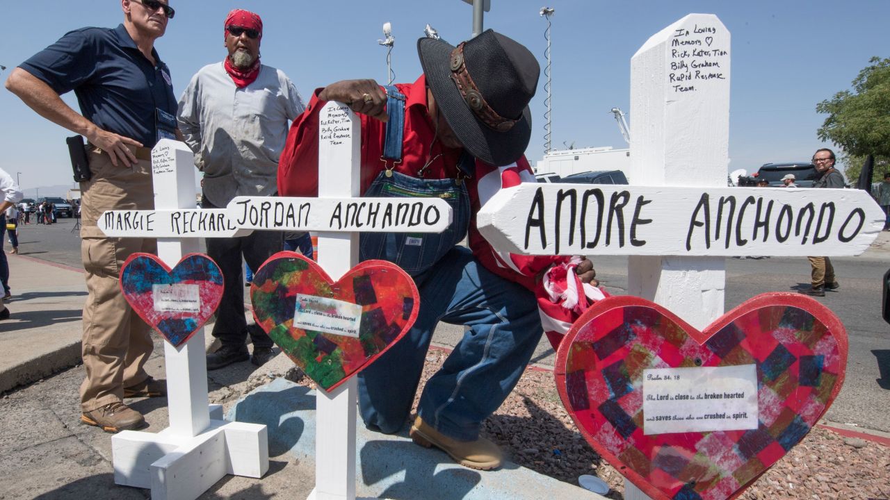 A man prays beside crosses bearing the names of Jordan and Andre Anchondo and the other victims of the El Paso massacre.