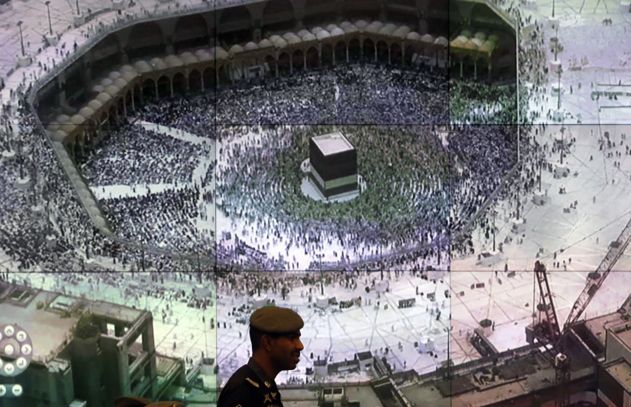 A Saudi police officer walks past a giant screen displaying the Kaaba.
