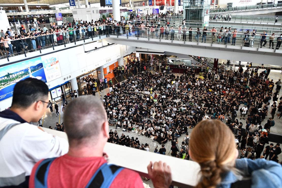 Tourists watch from above as protesters rally against a controversial extradition bill in the arrivals hall of Hong Kong's international airport on July 26, 2019. 