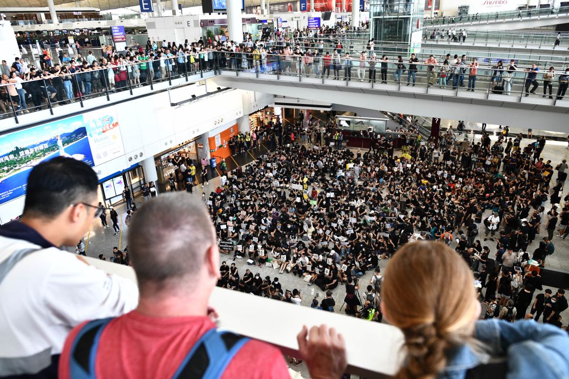 Tourists watch as protesters gather in the arrivals hall of Hong Kong international airport on July 26.