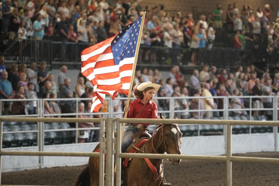 A young woman rides a horse while carrying the US flag.