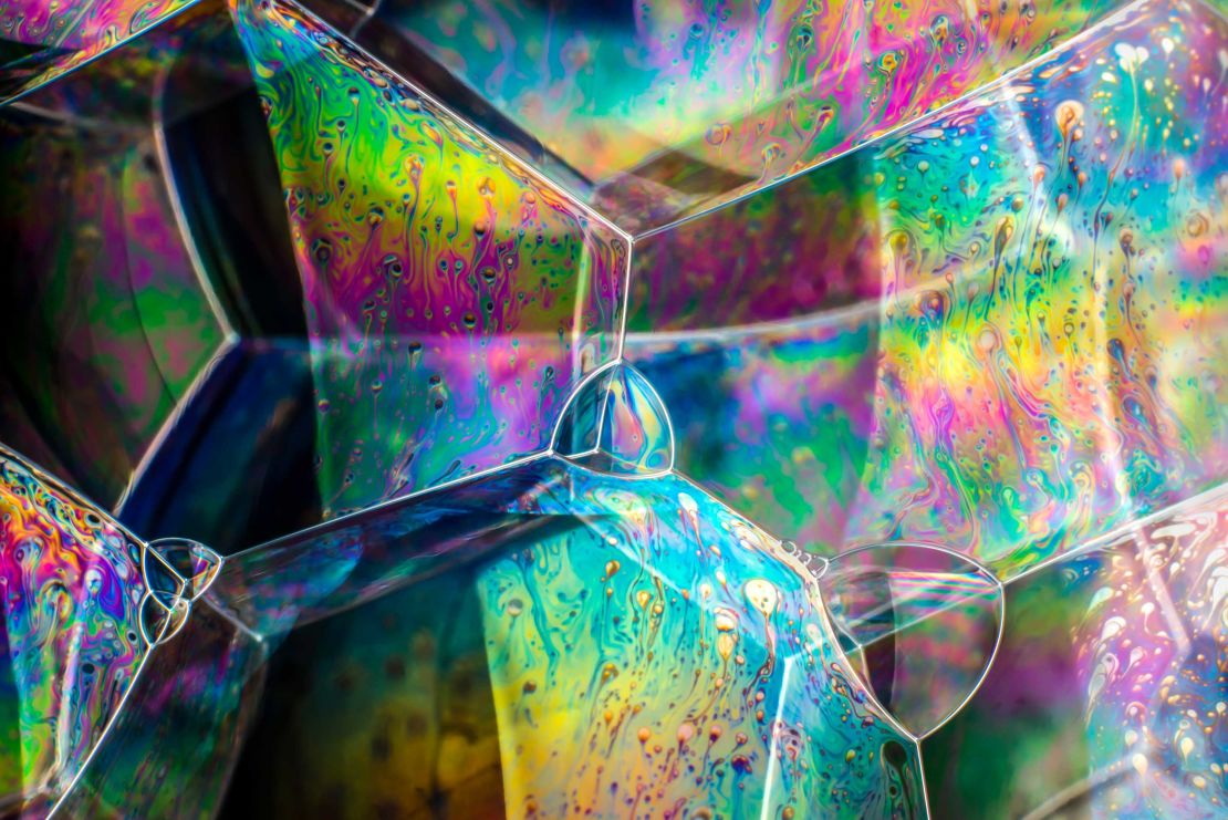 Soap Bubble Structures by Kym Cox. Bubbles want to optimise space and minimise their surface area for a given volume of air. This unique phenomenon makes them a reliable, useful tool in many areas of research. In particular, materials science and 'packing' -- how things fit together. Bubble walls drain under gravity, thin at the top, thick at the bottom and interferes with travelling lightwaves to create bands of colour. Black spots show the wall is too thin for interference colours, indicating the bubble is about to burst.