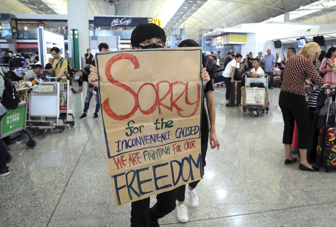 A protester shows a placard to stranded travelers during a demonstration at the Airport in Hong Kong, Tuesday, Aug. 13, 2019.