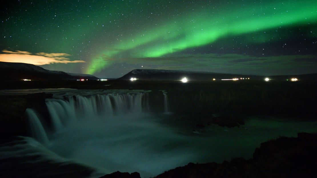 The northern lights appear over a waterfall in Iceland.
