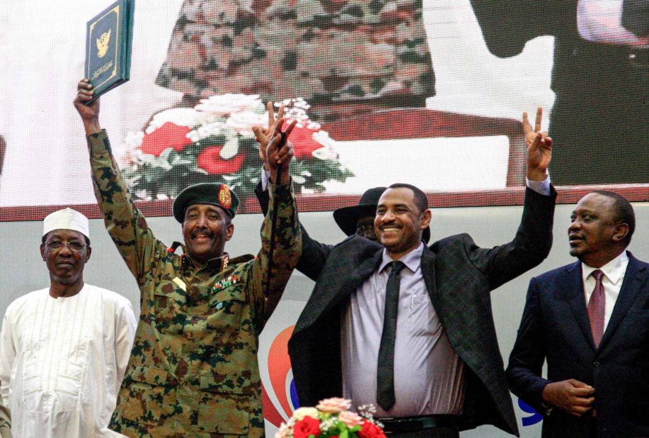 Sudanese protest leader Ahmad Rabie, center right, flashes the victory gesture alongside Gen. Abdel Fattah al-Burhan, the chief of Sudan's ruling Transitional Military Council, center left, during a ceremony where they signed a constitutional declaration.