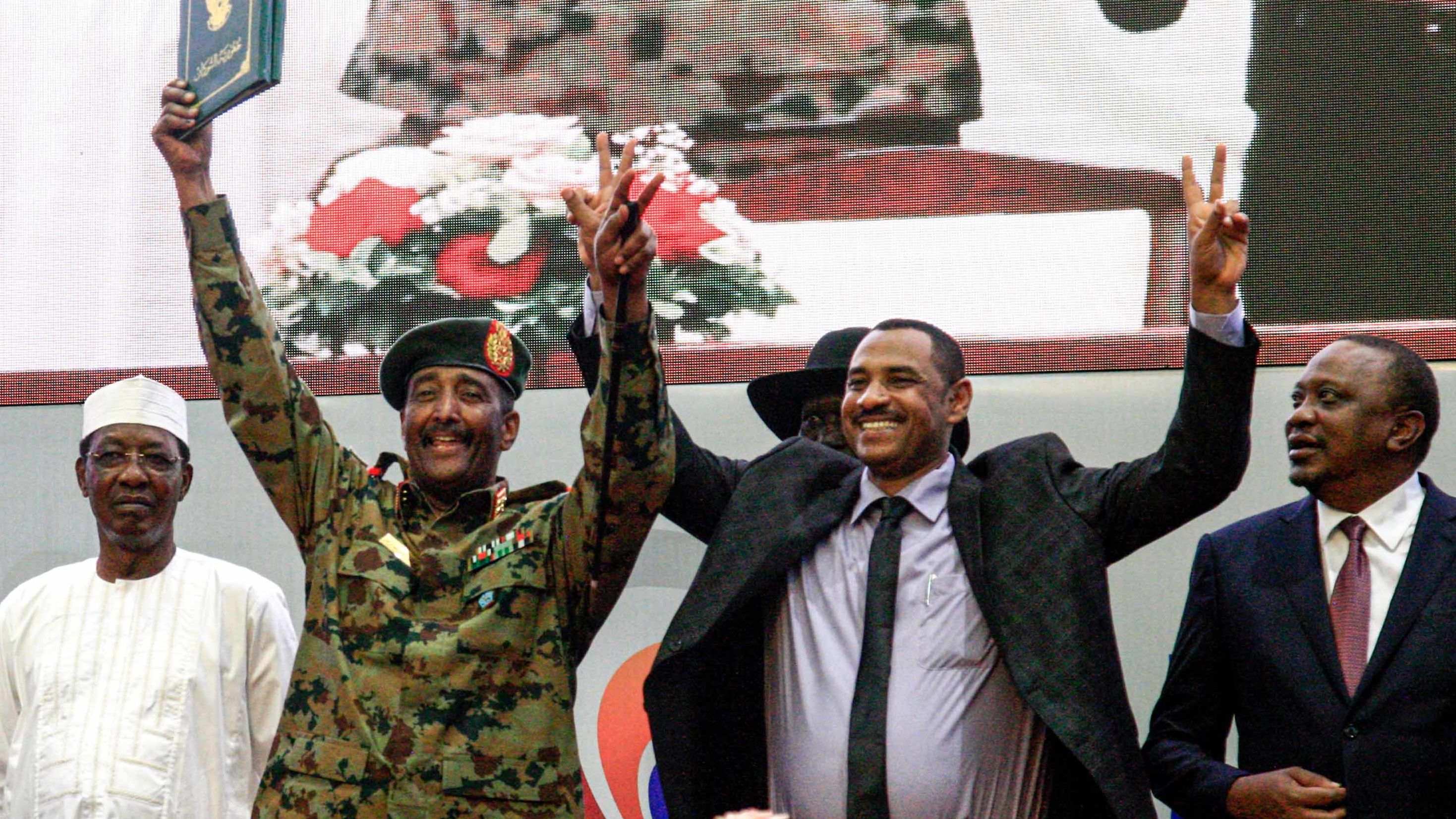 Sudanese protest leader Ahmad Rabie, center right, flashes the victory gesture alongside Gen. Abdel Fattah al-Burhan, the chief of Sudan's ruling Transitional Military Council, center left, during a ceremony where they signed a constitutional declaration.