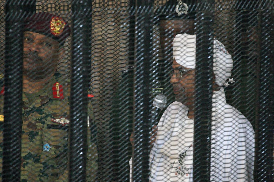 Bashir stands in a defendant's cage on the first day of his trial.