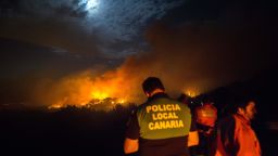 Firemen and policeman watch from the road as a blaze rages in Spain's Canary Islands on August 17, 2019. 