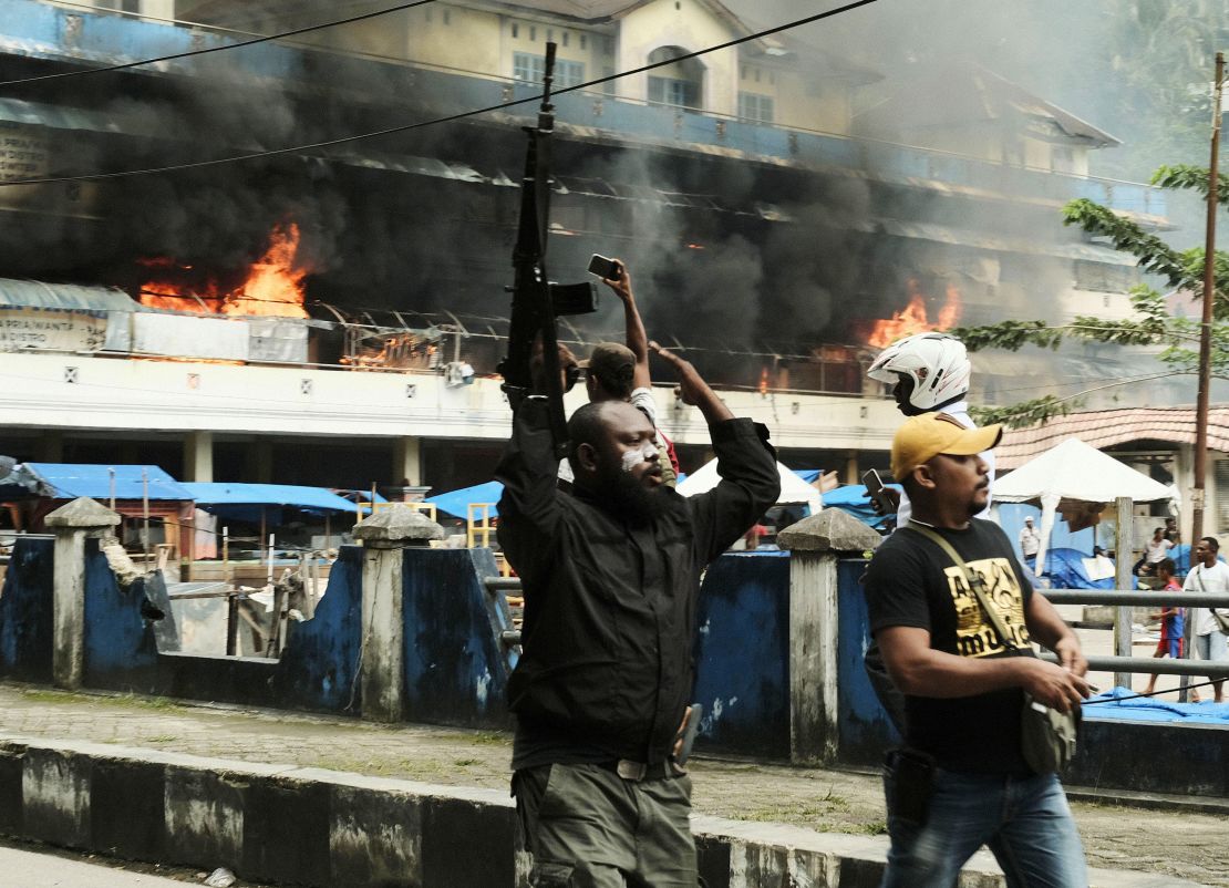 A police officer raises his rifle as the local market is seen burning during a protest in Fakfak in Indonesia's Papua province on Wednesday