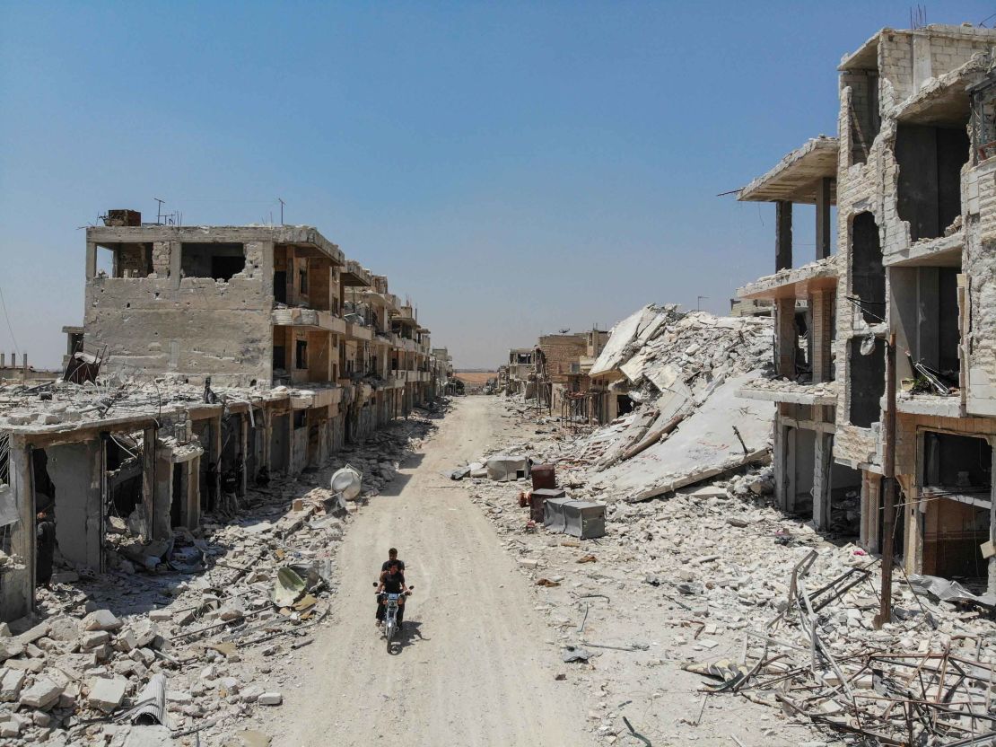An aerial view taken on August 3, 2019, shows Syrian men riding a motorcycle past the rubble of destroyed buildings in the town of Khan Sheikhoun.