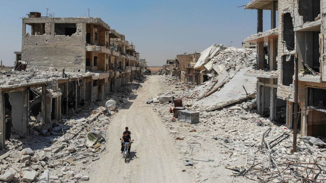 An aerial view taken on August 3, 2019, shows Syrian men riding a motorcycle past the rubble of destroyed buildings in the town of Khan Sheikhoun.