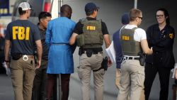 Federal agents hold a detainee, second from left, at a downtown Los Angeles parking lot after predawn raids that saw dozens of people arrested in the L.A. area Thursday, Aug. 22, 2019. U.S. authorities have unsealed a 252-count federal grand jury indictment charging 80 people with participating in a conspiracy to steal millions of dollars through a range of fraud schemes and laundering the funds through a Los Angeles-based network. The U.S. Attorney's Office says Thursday most of the defendants are Nigerian nationals. (AP Photo/Reed Saxon)