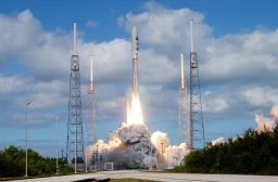 KENNEDY SPACE CENTER, FLA.  —   Into a cloud-scattered blue sky, NASA's New Horizons spacecraft roars off the launch pad aboard an Atlas V rocket spewing flames and smoke.  Liftoff was on time at 2 p.m. EST from Complex 41 on Cape Canaveral Air Force Station in Florida. This was the third launch attempt in as many days after scrubs due to weather concerns.   The compact, 1,050-pound piano-sized probe will get a boost from a kick-stage solid propellant motor for its journey to Pluto. New Horizons will be the fastest spacecraft ever launched, reaching lunar orbit distance in just nine hours and passing Jupiter 13 months later. The New Horizons science payload, developed under direction of Southwest Research Institute, includes imaging infrared and ultraviolet spectrometers, a multi-color camera, a long-range telescopic camera, two particle spectrometers, a space-dust detector and a radio science experiment. The dust counter was designed and built by students at the University of Colorado, Boulder. The launch at this time allows New Horizons to fly past Jupiter in early 2007 and use the planet's gravity as a slingshot toward Pluto. The Jupiter flyby trims the trip to Pluto by as many as five years and provides opportunities to test the spacecraft's instruments and flyby capabilities on the Jupiter system. New Horizons could reach the Pluto system as early as mid-2015, conducting a five-month-long study possible only from the close-up vantage of a spacecraft.