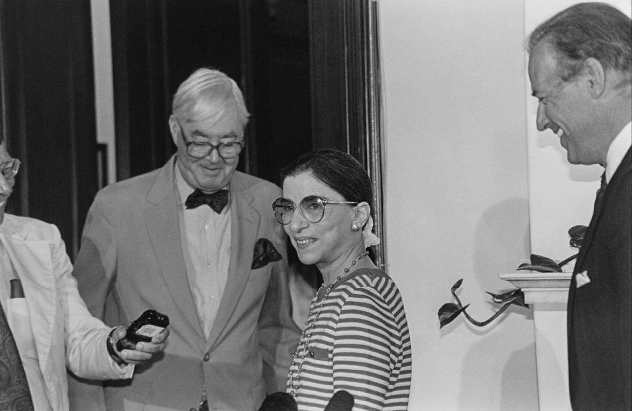 Ginsburg talks with a reporter after being nominated for the Supreme Court in 1993. On the far right is US Sen. Joe Biden. US Sen. Daniel Patrick Moynihan is wearing the bowtie.