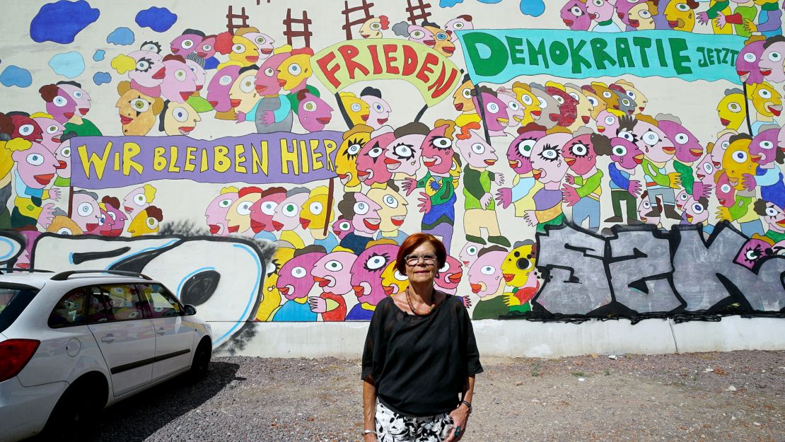 Retired Greens MEP, Gisela Kallenbach, poses in front of a mural depicting the 1989 protests.