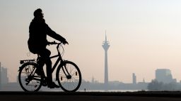 A man rides a bicycle along the Rhine River as the Rheinturm telecommunications towers stands behind on February 20, 2018 in Dusseldorf, Germany.