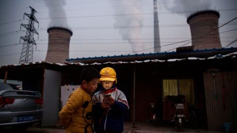  Chinese boys look at their smartphone in front of their house next to a coal fired power plant on the outskirts of Beijing, China.