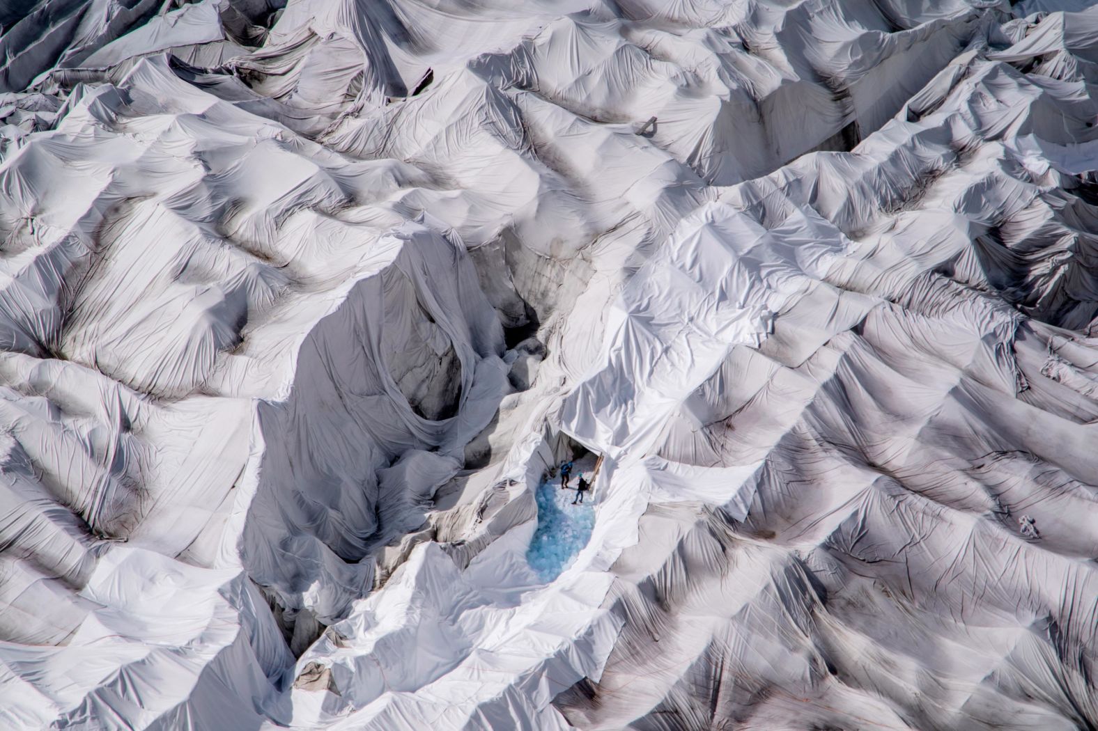 Two people are seen at an ice cave entrance on the Rhone Glacier in the Swiss Alps. Every summer, the glacier is covered with huge sheets of white fleece blankets to slow down its melting, according to photographer <a href="index.php?page=&url=https%3A%2F%2Fellingvag.photoshelter.com%2Findex" target="_blank" target="_blank">Orjan F. Ellingvag.</a> "The fleece-covered cave attracts more and more tourists worried about global warming and wanting to see the remnants of a dying glacier," Ellingvag said.