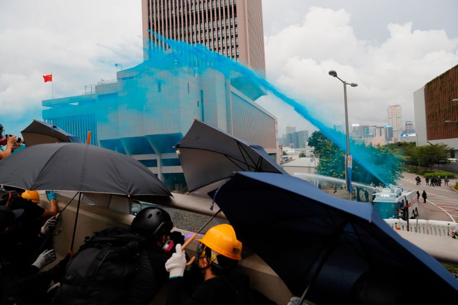 Protesters take cover as policemen fire blue-colored water on them. Blue dye can be used to stain and identify masked protesters.