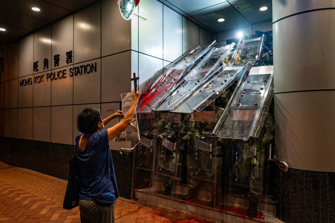 A woman holds a cross in front of the Mongkok Police Station as riot police holding shields stand guard during a standoff with protesters after an anti-government rally in on September 1, 2019, in Hong Kong.