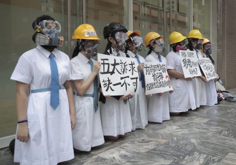 Students wearing gas masks and helmets hold a banner that reads 