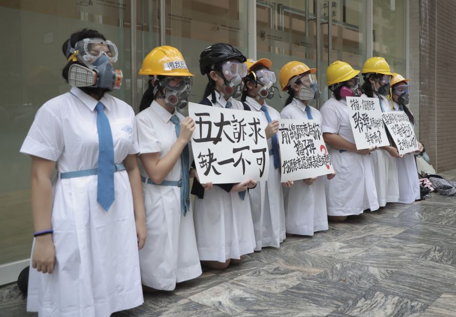 Students wearing gas masks and helmets hold a banner that reads "five major demands are indispensable" at St. Francis' Canossian College in Hong Kong.