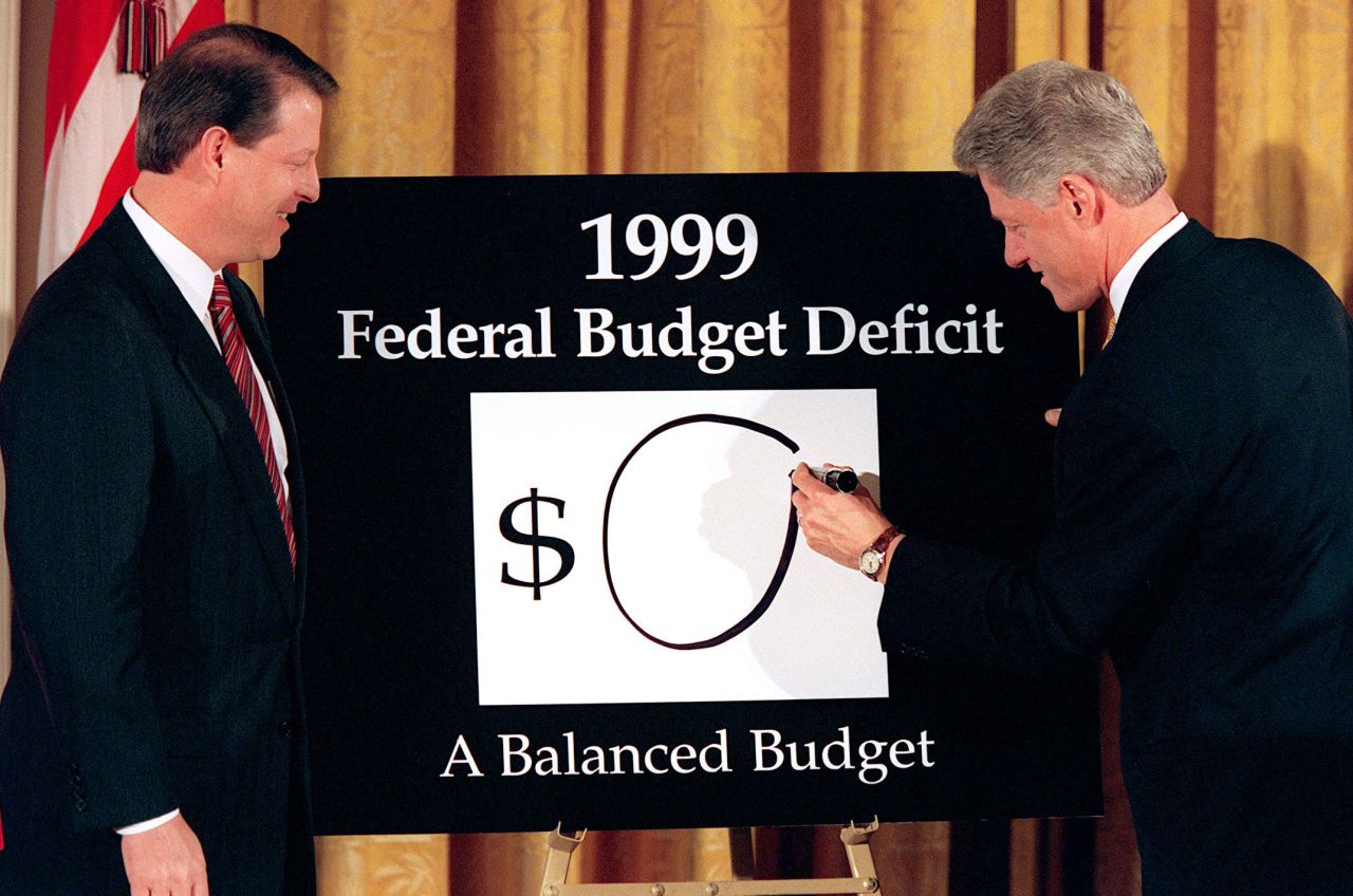 Vice President Al Gore looks on as Clinton writes a "0" on the board, showing what the federal deficit would be after unveiling his balanced budget plan for 1999. The President declared an end to "an era of exploding deficits" as he sent a $1.73 trillion budget to Congress that promised the first surplus in more than three decades.  