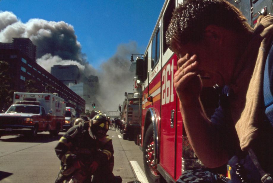 A New York firefighter pauses as smoke rises in the background.