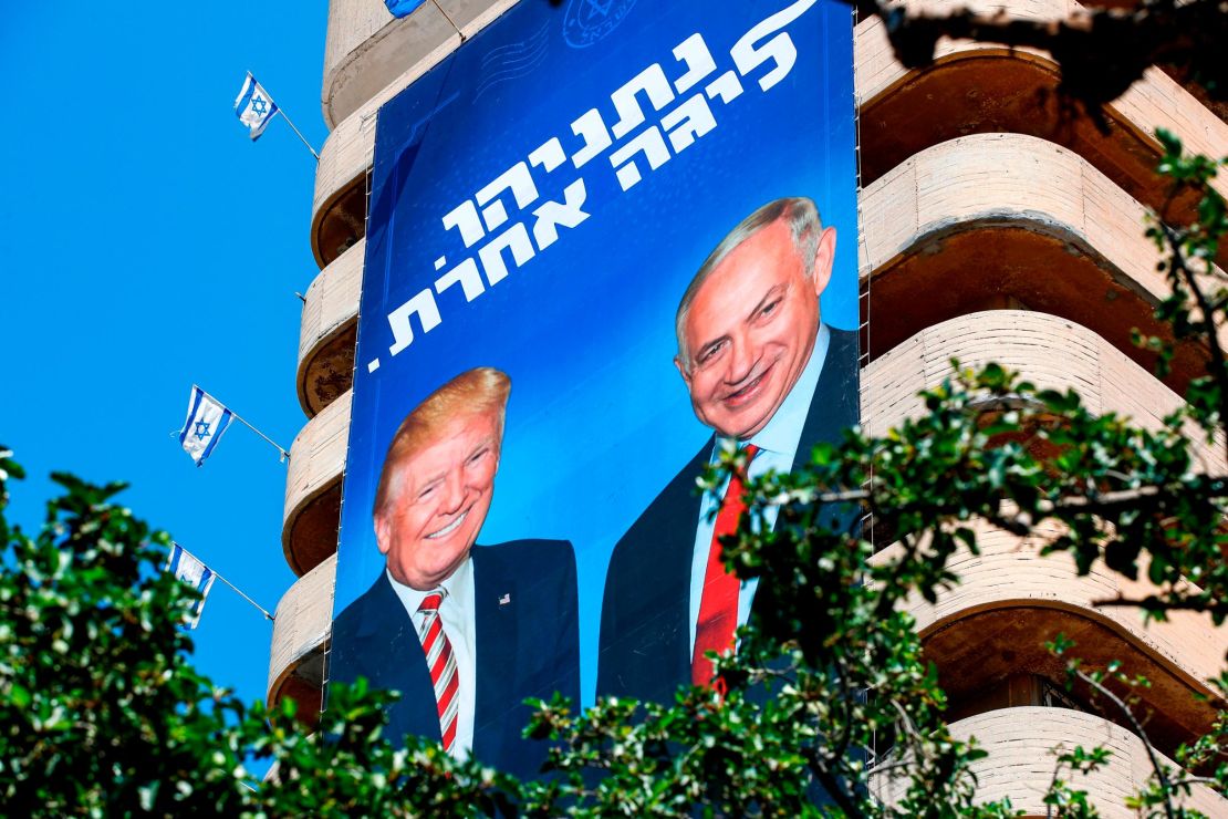 A giant Israeli Likud Party election banner hangs from a building in Tel Aviv showing Netanyahu shaking hands with Trump, with a caption above reading in Hebrew "Netanyahu, in a league of his own."