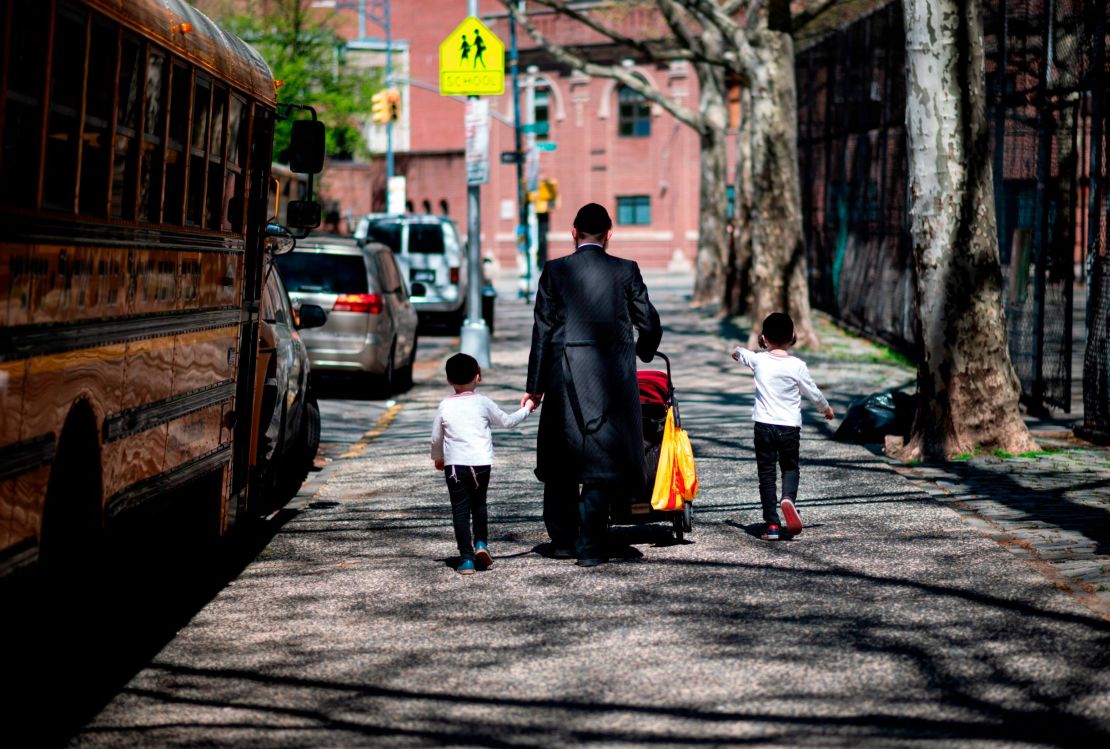 A Jewish man walks with his children down a street in Williamsburg, Brooklyn.