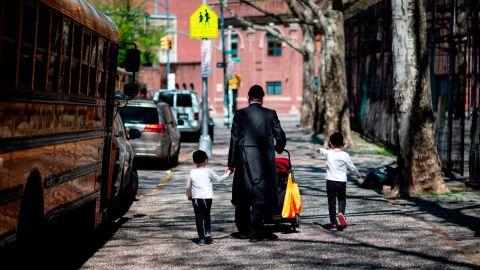 A Jewish man walks with his children down a street in Williamsburg, Brooklyn.